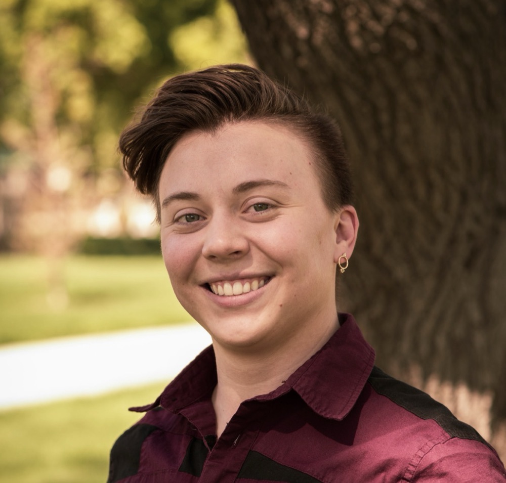 Portrait of Max Keate, smiling, outdoors beside a tree