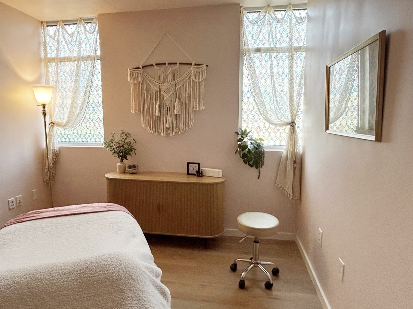 The treatment room with a woven sideboard, plants and a mirror catching the window light